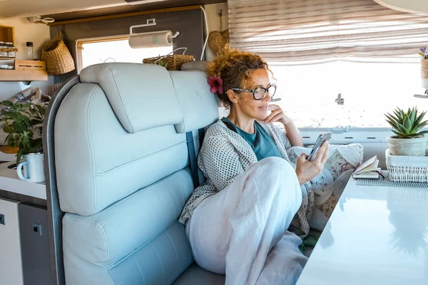 Adult woman relaxing inside a modern luxury camper van rv vehicle motor home reading notification on cell phone. Alternative home vanlife style and tourism renting van. Tiny house. Traveler lifestyle