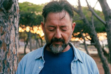 Üzgün adam portresi yüz ifadesi açık hava parkına yakın. Gözleri kapalı yetişkin bir erkek aşağı bakıyor. Hayatla ilgili sorunlar. Zihinsel çöküntü. Depresyon ve terapi. Hayat sıkıntısı olan kişi