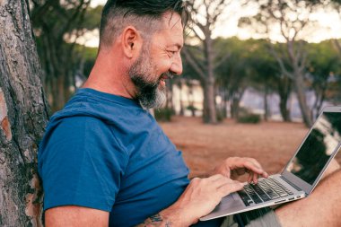 Parkta, açık hava doğa ofisindeki insanlar çalışıyor. Mutlu adam özgürlüğün ve küçük online işlerin tadını çıkarıyor. Kablosuz bağlantı. Küçük işletmeler için dizüstü bilgisayar kullanmak