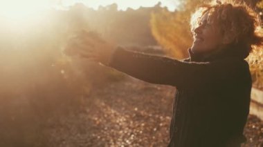 Kış geliyor. Sonbahar günbatımı ve mutlu kadın havaya yapraklar fırlatıyor kollarını açıyor ve mutlulukla gülümsüyor. Huzurlu insanlar ve doğal sağlıklı yaşam tarzı. Açık hava aktivitesi yapan bayan.
