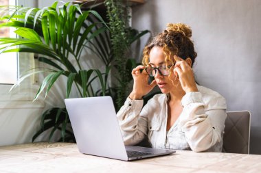 Şakaklara masaj yapan yorgun bir kadın, bilgisayardan sonra baş ağrısı çeken, dizüstü bilgisayarla evde oturan, başına dokunan yorgun genç bir kadın, baş ağrısını dindiren bir migren.
