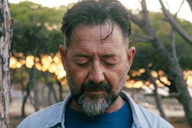 Üzgün adam portresi yüz ifadesi açık hava parkına yakın. Gözleri kapalı yetişkin bir erkek aşağı bakıyor. Hayatla ilgili sorunlar. Zihinsel çöküntü. Depresyon ve terapi. Hayat sıkıntısı olan kişi