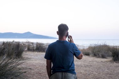 Arka planda duran bir adamın, okyanus ve adanın bulunduğu seyahat manzaralı bir arka planda cep telefonu kullanırken görüntüsü. İnsanlar turist ve cep telefonu teknolojisi kablosuz bağlantıları