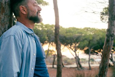  Bir ağaç gövdesine karşı duran bir adam parkta tek başına boş vakitlerde rahatlıyor. İnsanlar ve refah doğa ile bağlantılıdır. Rahatla zihinsel dingin ifade insanı olgun