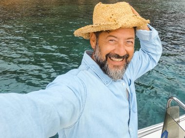 Yüzünde heyecanlı bir ifade olan neşeli mutlu bir adam yaz tatili seyahatinde bir teknenin içinde durup selfie çekiyordu. Erkek insanlar hayattan ve turizmden zevk alıyorlar