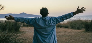 Adam açık havada kollarını doğa manzarası ve açık gökyüzü önünde uzatıyor. Özgürlük ve seyahat kavramı, sağlıklı yaşam tarzı dengeli zihinsel durum. Turistler eğleniyor