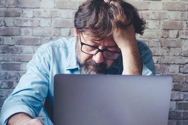 Dizüstü bilgisayarın önünde eli başında endişeli bir adam stresli ve endişeli bir ifadeyle ekrana bakıyor. İşte kötü sorunlar. Çevrimiçi güvenlik hackleme. - Evet. Akıllı çalışan modern insanlar.
