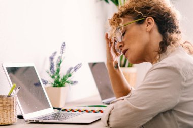 Ev işyerindeki dizüstü bilgisayarın önünde boyuna ve gözlüklerine dokunan yorgun bir kadın. Küçük online bilgisayar teknolojisi modern insanların yaşam tarzı kavramı. Stres ve sorunlar defter işi