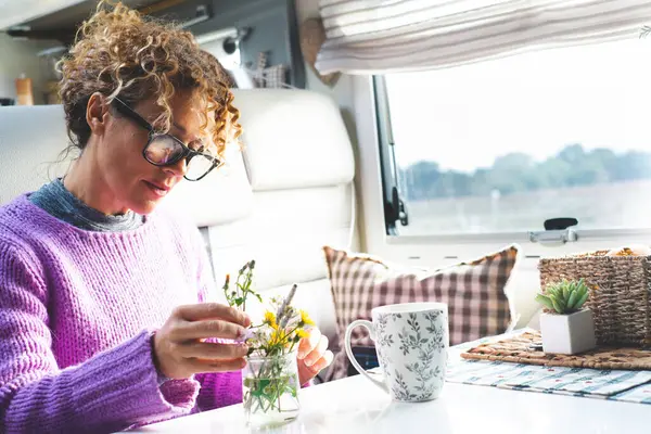 woman caring plants and flowers inside a camper van modern tiny house motorhome rv alone. People living van life full time. People and nature. Happy young mature female indoor leisure