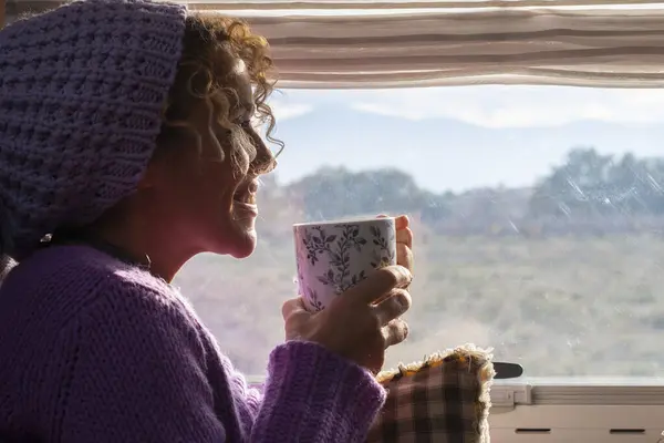 woman side view smile and enjoy travel lifestyle and destination drinking coffee and admiring the view outside the widow of her camper van. Van life. Alternative vehicle travel vacation people