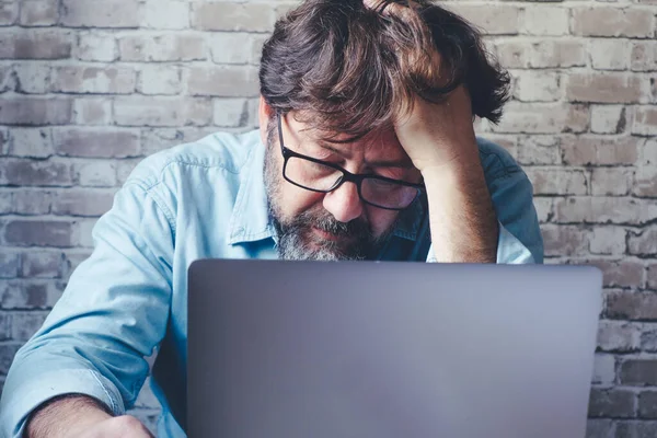 worried man in front of a laptop with hand on his head looking the display with stressed and worried expression. Bad problems at work. Online security hack. . Smart working modern people indoor