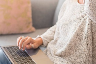 Kanepede oturan bir kadının dizüstü bilgisayarını kullanarak elini kapat. İnternette tek başına sörf yapmak, ev içi eğlence teknolojisi aktiviteleri. İnsanlar ve defter. Sosyal medya sohbeti. Çevrimiçi etkinlik