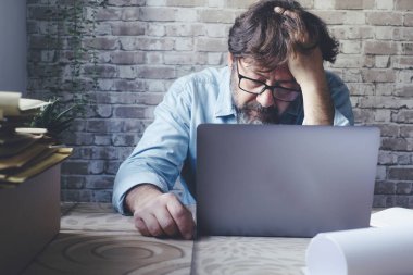 Dizüstü bilgisayarın önünde eli başında endişeli bir adam stresli ve endişeli bir ifadeyle ekrana bakıyor. İşte kötü sorunlar. Çevrimiçi güvenlik hackleme. - Evet. Akıllı çalışan modern insanlar.