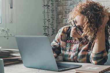 Modern serbest girişimci kadın evinde, küçük iş yerindeki dizüstü bilgisayarında çalışıyor kafasına dokunuyor ve bilgisayar ekranına şüpheyle ve merakla bakıyor. Çevrimiçi kadın insanlar