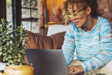 Kanepede dizüstü bilgisayarla çalışan orta yaşlı bir kadın - teknoloji online insan yaşam tarzı konsepti - akıllı çalışan ya da dijital iş aktivitesi yapan yetişkin bir kadın