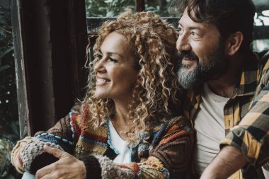 Bir çift yetişkin erkek ve kadın evde oturup pencereden dışarı bakarak eğleniyor ve rahatlıyorlar. Aşık genç insanlar ve ilişki konsepti yaşam tarzı