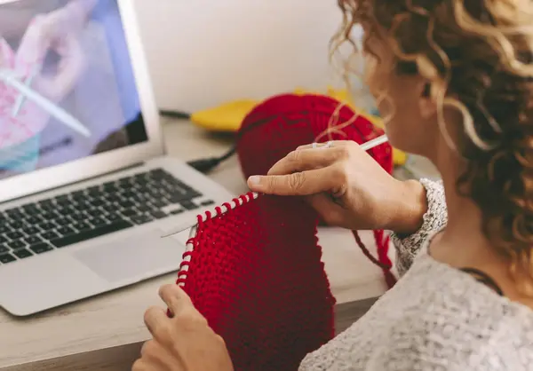 Woman at home doing knit work watching online tutorial class lesson on laptop computer online. Modern work female people activity with internet connection. Woolen yarn knitting hobby indoor