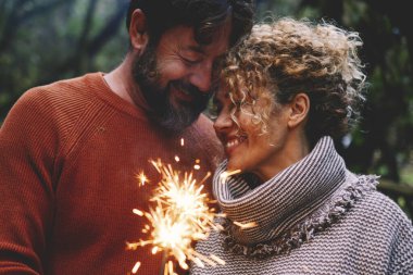 Romantik yetişkin çift, orman yeşil ağaçlarının arka planında alevli ışık eşliğinde sevişip eğleniyor. Şefkatli ve şefkatli bir erkek ve kadın bunu ateş ışığı ve gülümsemeyle kutluyor.