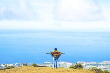 Turist ve özgürlük yaşam tarzı insanlar seyahat konsepti. Kollarını açıp muhteşem manzaranın ve manzaranın tadını çıkaran bir kadın. Uçurumun tepesinden mavi okyanus ve gökyüzü. Mutlu bayan.