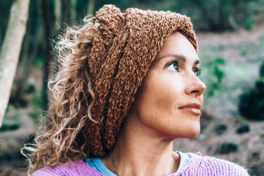 Boş günlerinde gülümseyen ve parka bakan orta yaşlı güzel bir kadının portresi. Gülümseyen bir kadının açık hava portresi. Güzel saç bandıyla parkta eğlenen neşeli bayan..