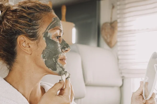 adult woman applying cream beauty skin treatment mask on face using a mirror. Camper van lifestyle and healthy care female people activity. Pretty lady caring herself for aging