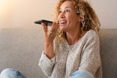 Evdeki telefon görüşmesinde telefonda konuşan heyecanlı bir kadın kanepede oturuyor. Kapalı alan aktivitesi ve modern cihaz kullanımı. Dişi insanlar arkadaşlarıyla ses bağlantısından zevk alıyorlar. 