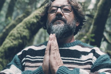 Olgun sakallı adam portresi yeşil bir ortamda meditasyon yapar. Güzel bir orman. Açık doğa parkında meditasyon yapan yaşlı bir erkek. Gözleri ve elleri kapalı. Huzurlu bir hayat