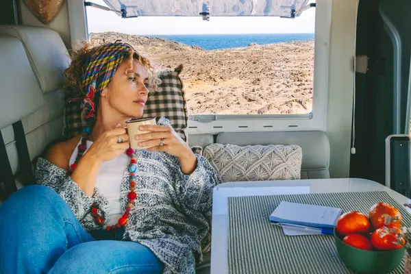 Cute  adult woman have relaxed leisure activity laying on the sofa inside her cozy alternative home camper van. Concept of tourism and modern van life. Beach and ocean view outside the window