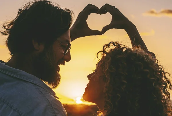 Peace and love with couple doing heart gesture sign with both hands together. Sunset light and outdoor romantic activity with adult man and woman enjoying relationship.