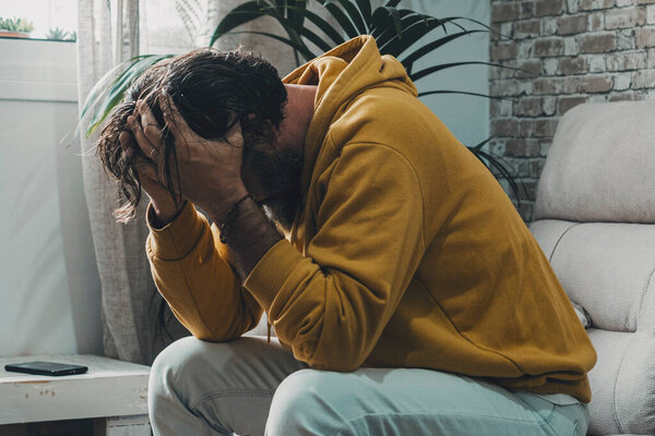 man alone at home holding his head with desperation and frustration. Concept of stressed people indoor. Over worried and problems to solve. Bad day. Economy crisis and bankrupt family situation