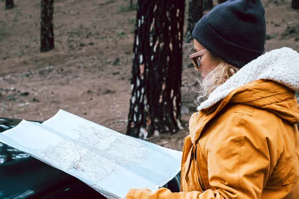 Woman check paper map in the woods forest on the front of the black off-road car - concept of people and adventure lifestyle - travel wanderlust, life with independent female lost in the outdoors park