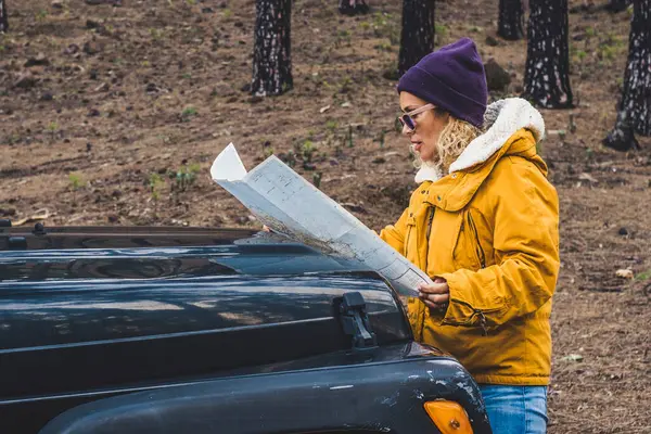 Woman check paper map in the woods forest on the front of the black off-road car - concept of people and adventure lifestyle - travel wanderlust, life with independent female lost in the outdoors park
