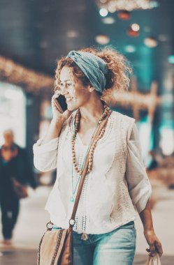  Kadın gülümsüyor ve alışveriş merkezinin içinde yürüyor mağazalara ve kıyafetlere bakıyor. Alışveriş etkinliği, kadın insanlar alışveriş merkezinde indirimli tatil sezonunu severler. Arkadaşlarını aramak için telefon kullanıyorsun.