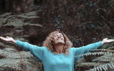 happy woman enjoy nature and park outstretching arms and looking in the air with happiness and joy. Outdoor leisure activity for free female people alone in the woods. Green environment background clipart