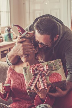 Mutluluk ve noel kutlaması zamanı. Bir adam, karısına gözlerini kapayarak sürpriz yapıyor. Mutlu kadın Noel tatili için hediye alıyor. Aralık kutlaması.