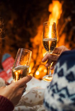 Arka planda, arka planda şömine olan şampanya kadehleriyle eğlenen ve kutlama yapan çiftin görüntüsü. Kış tatili ve aşk ilişkisi. Yılbaşı arifesi