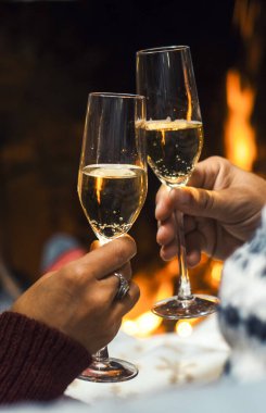 Romantik çiftin, birlikte kutlama yaparken, aşk ve ilişkide şampanya kadehleri içerken yakın plan görüntüsü. İnsanlar yeni yıl arifesini şömine önünde kutluyor.