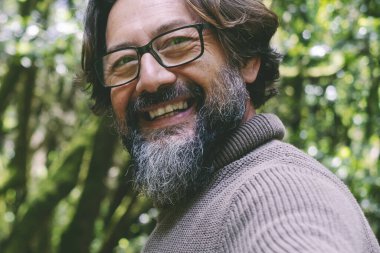  Adam gülüyor ve arka planda yeşil doğa ağaçları ve ormanla eğleniyor. İnsanlar arkadaşlarıyla ya da yalnız başlarına ulusal park ormanlarının keyfini çıkarıyorlar. Çevre ve alternatif eğlence etkinliği