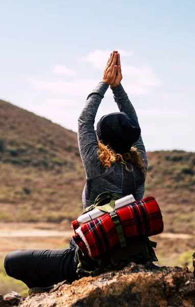 Back view of adventure woman doing yoga healthy position in front of a mountain in outdoor trekking activity alone. Hiking and zen meditation lifestyle concept. Female people travel alternative
