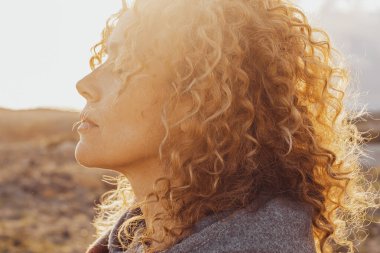Çekici bir kadının yan görünüş portresi. Gözlerini kapayan ve doğa ile eğlenen yalnız başına boş zaman aktivitesi. İnsanlar ve tefekkür meditasyonu. Sakin bir yaşam tarzı, kadın kişiliği. Uzun kıvırcık, sağlıklı saçlar.