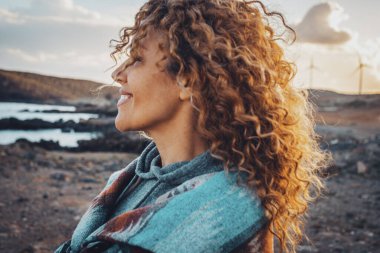 Dışarıda gülümseyen uzun kıvırcık saçlı bir kadın yalnız başına eğleniyor. Seyahat ve turizm insanları kavramı. Mutluluk açık havada boş zaman aktivitesi. Sakin bir yaşam tarzı. Hedef