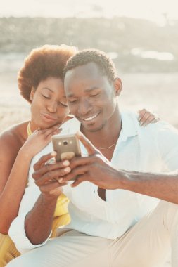 Siyah çift genç adam ve kadın cep telefonu ve uygulama kullanarak iletişim teknolojisinden zevk alıyorlar. Mutlu modern insanlar akıllı telefondan yazıyorlar. Birlikte eğleniyorlar ve gülümsüyorlar.