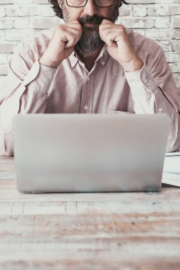 Front view of man working at the desk with laptop and paper charts. Concept of business and job activity alone. Wooden table with people using computer to manage company. One worker thinking indoor