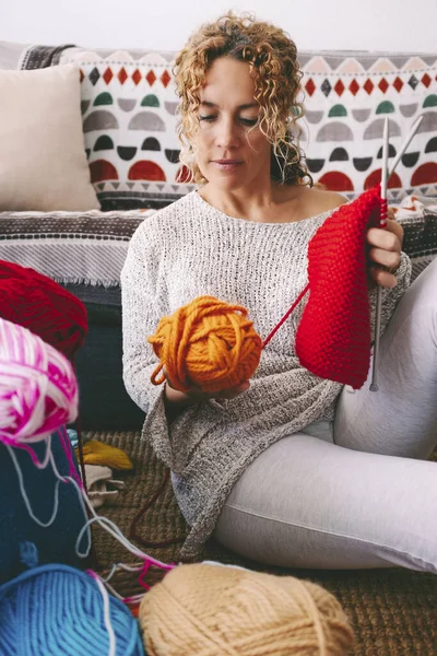 woman at home sitting on the ground busy in knitting hobby work activity. Indoor leisure female people with wool. Creative time concept. Learning new things. Adult lady spending time in apartment