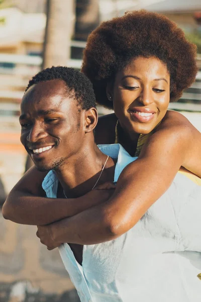 Happy black people couple with young man and woman having fun together in piggyback carrying activity.  african male and female enjoying leisure. Buildings houses in background. Love friends