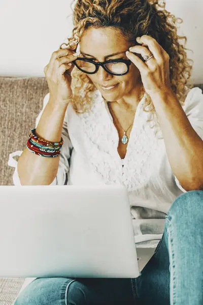 modern woman at home working happy on a laptop sitting on the sofa. Online job person using computer with a smile. Pretty female people surfing the web alone at home with glasses