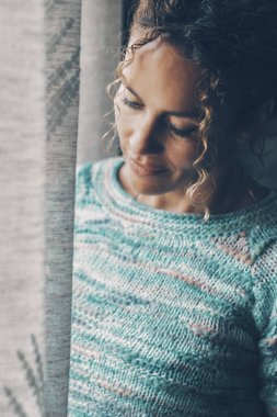 View of a woman alone at home near the window. Concept of serene people smiling ad thinking happy. Blue image mood. Middle age lonely female with closed eyes enjoying life and lifestyle indoor