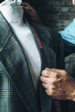 Close up of tailor at work in the workshop taking measures of an elegant suit blazer. Man working in tailoring business activity alone. Concept of people and job handmade. One worker indoor activity