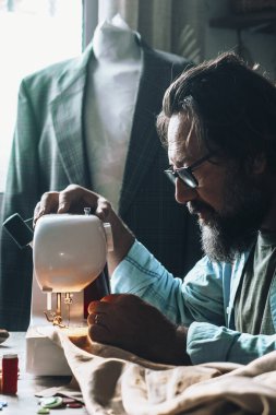 Evde çalışan bir adam dikiş makinesini sadece eski giysiler üzerinde çalışmak için kullanır. Erkek insanlar içeride terzi olarak çalışıyor. Alternatif iş yeri konsepti yaşam tarzı.