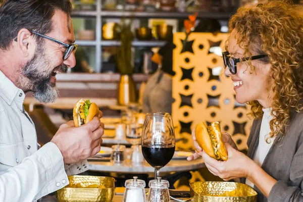 ハッピーカップル笑顔とハンバーガーとチップを食べるパブレストランで話す カフェバーでランチ休憩をしている夫婦 週末に出かける男性と女性とのライフスタイルのコンセプト — ストック写真